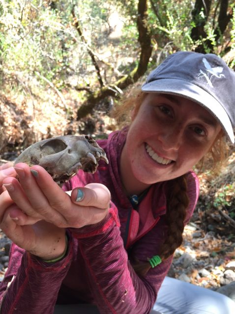 Smiling girl in baseball cap and pink sweater holds a small animal skull