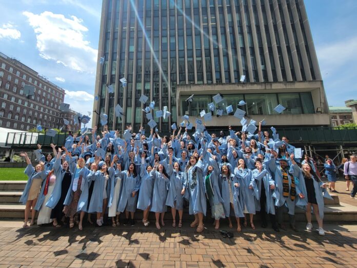 large group of students in blue gowns throwing graduation caps