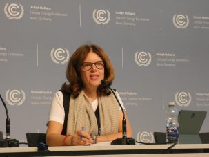 Woman wearing scarf sits opposite a microphone.