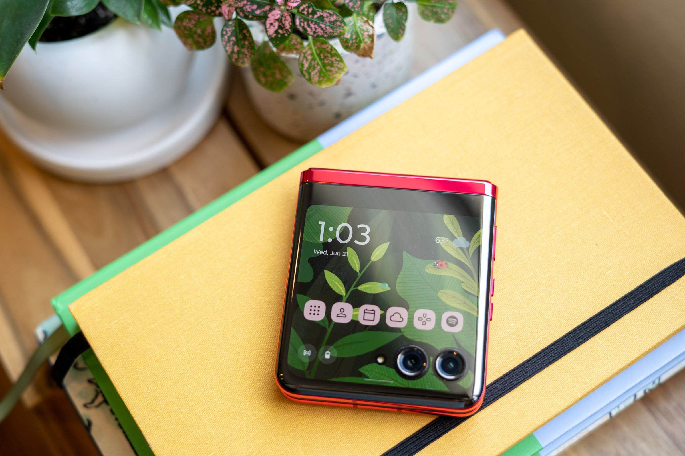 Motorola Razr Plus on a stack of books with cover screen on showing illustrated home screen background.