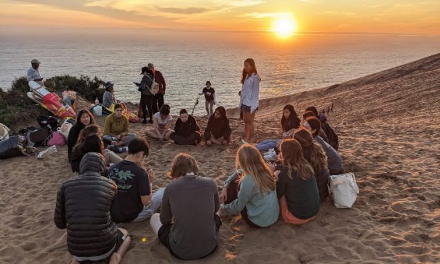Group of students on a beach with the sun in the background