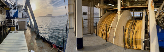 Panorama of the Langseth and its multichannel streamer reels with mountains along Mexican coastline in the background.