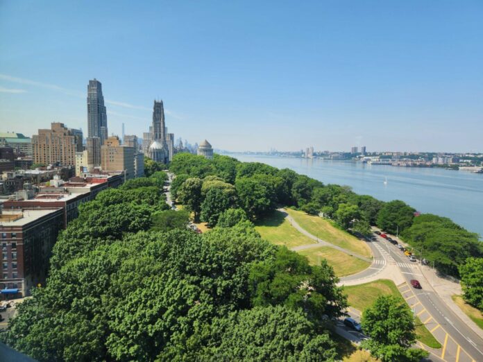 Aerial view of tree-covered NYC parkland and Hudson River. 